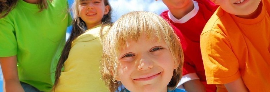 Kinder in bunten T-Shirts, ein Kind lächet im Vordergrund in die Kamera. 