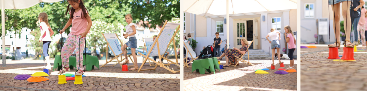 Belebter Vorplatz des Bildungshauses im Sommer: Liegestühle laden zum Verweilen ein, Kinder nutzen die angebotenen Spielsachen.